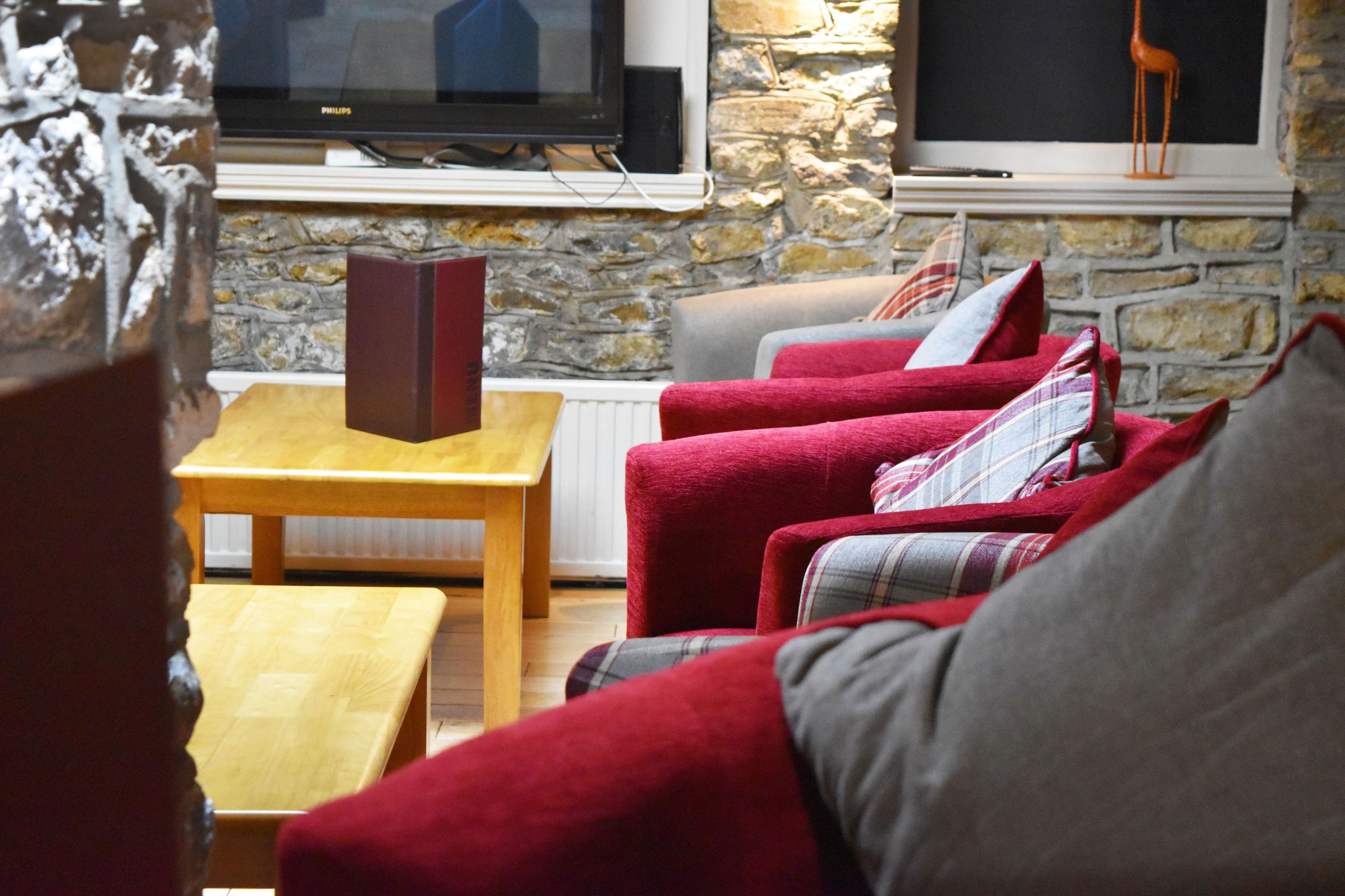 Un salón acogedor con pared de piedra, un televisor de pantalla plana, sofás rojo y gris, y una mesa de centro de madera.