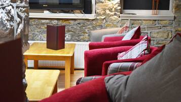 Un salón acogedor con pared de piedra, un televisor de pantalla plana, sofás rojo y gris, y una mesa de centro de madera.