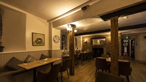 A cozy restaurant with wooden tables and chairs, a stone wall, and a fireplace. - The Swan Hotel (Wotton-under-Edge)