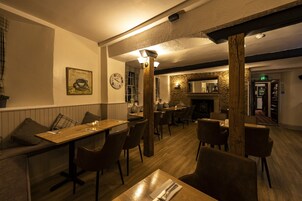 Un restaurante acogedor con mesas y sillas de madera, una pared de piedra y una chimenea.