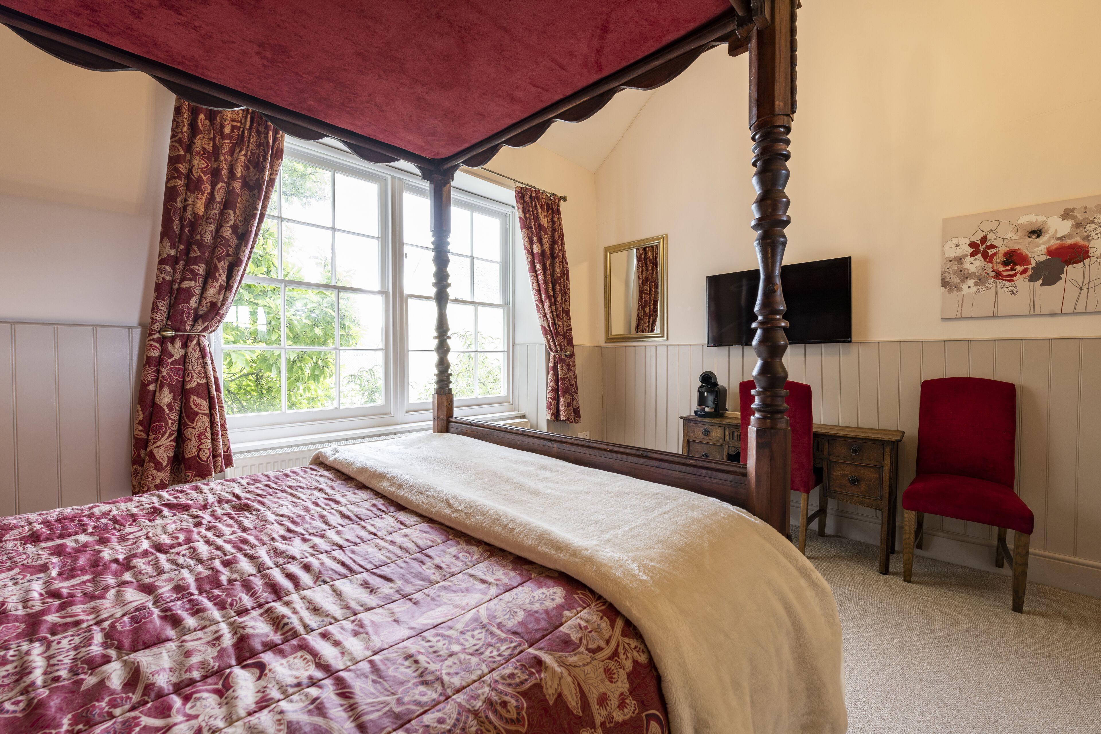 A bedroom with a four-poster bed, a television, a red chair, and a painting on the wall.