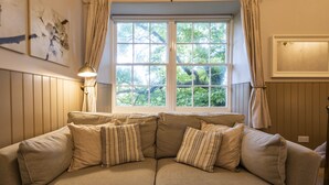 A beige sectional sofa with striped pillows, a floor lamp, and a window with curtains. - The Swan Hotel (Wotton-under-Edge)