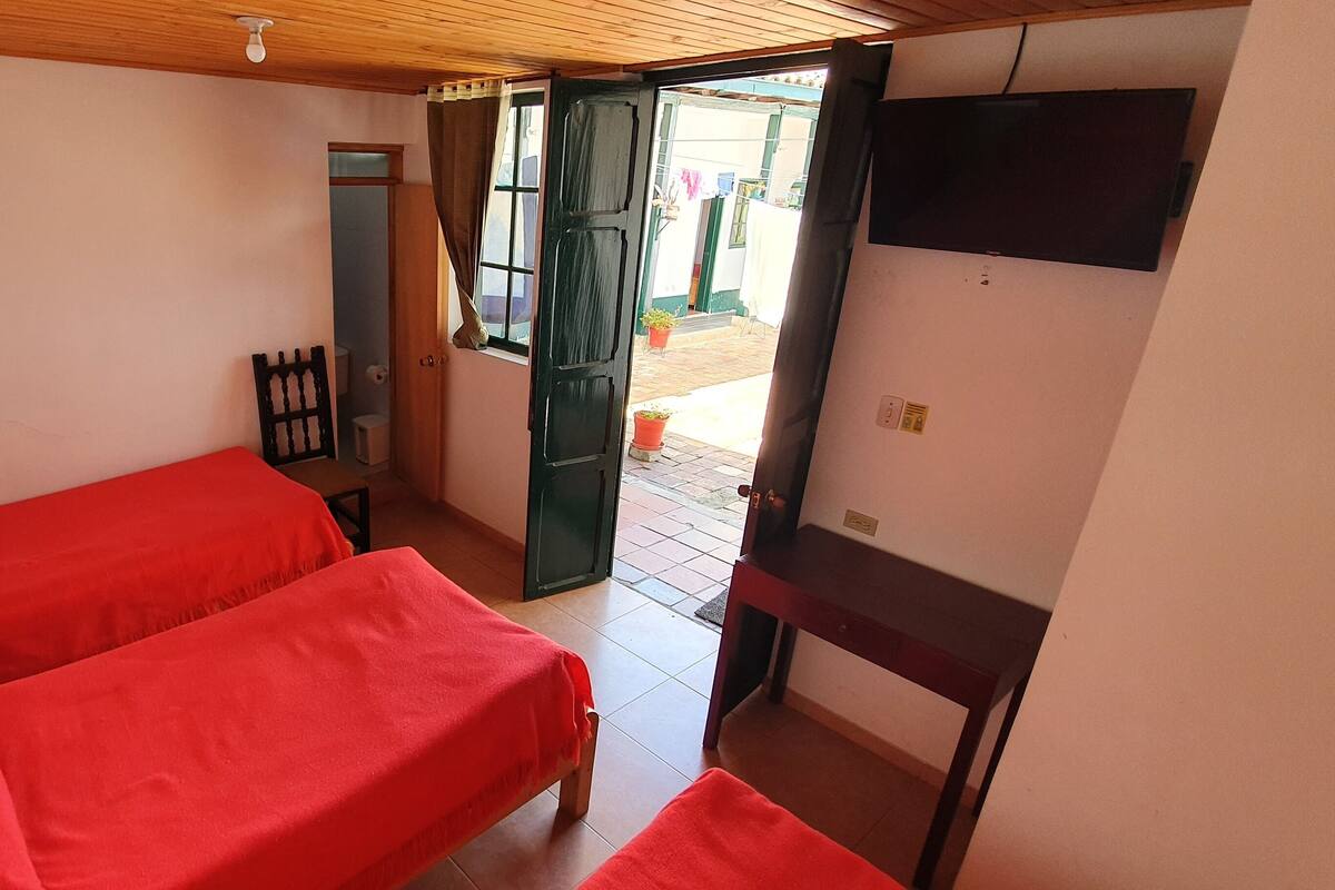 Una habitación con dos camas, techo de madera, televisor montado en la pared y puerta abierta que da al exterior.