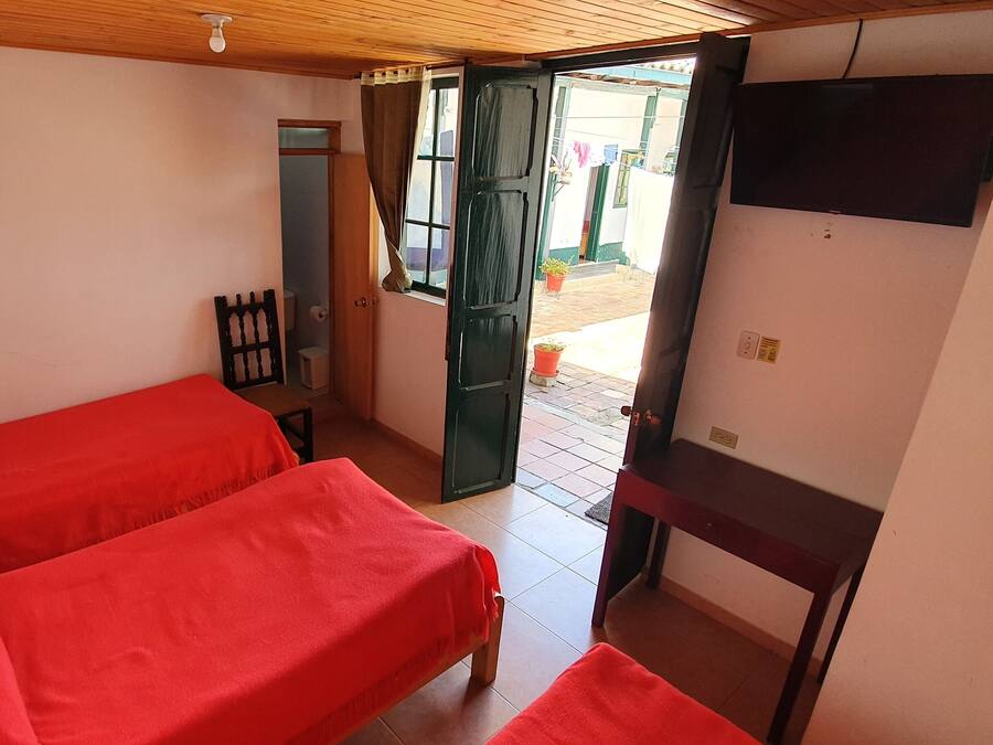 Una habitación con dos camas, techo de madera, televisor montado en la pared y puerta abierta que da al exterior.