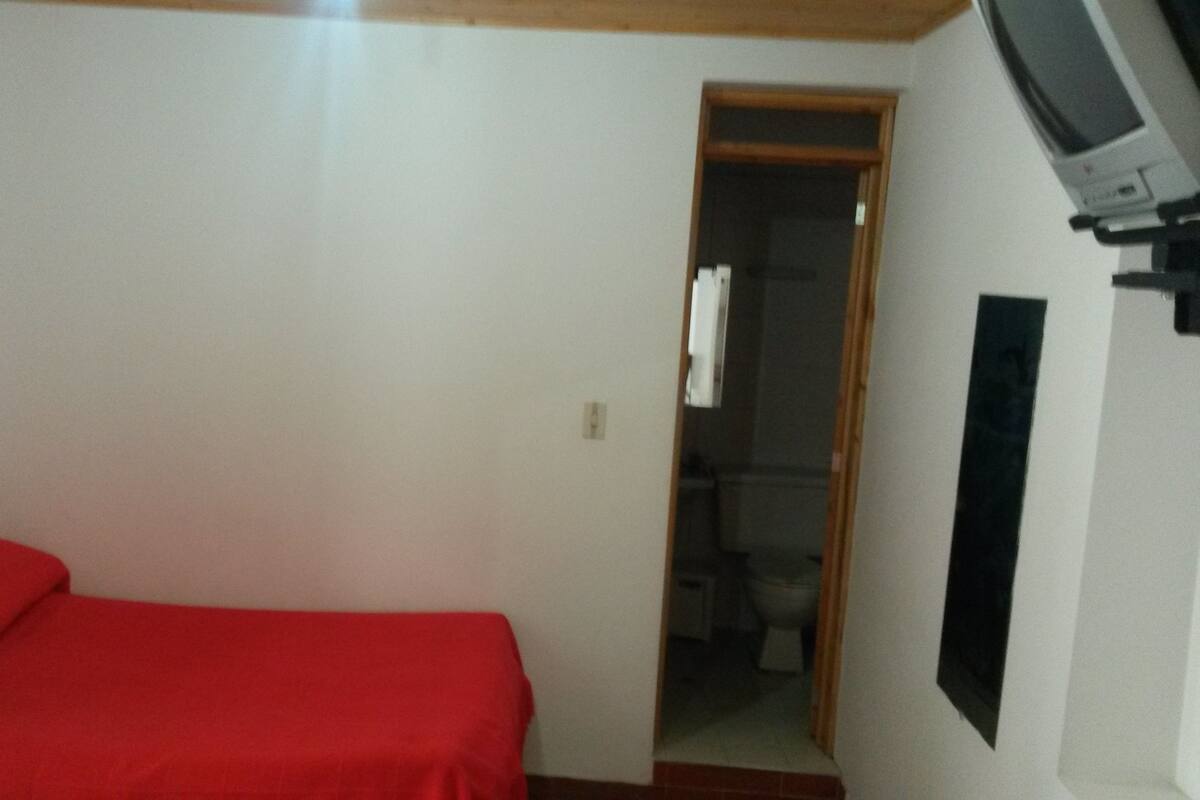 Una habitación pequeña y con pocos muebles, con una cama individual, una puerta que da al baño y un televisor montado.
