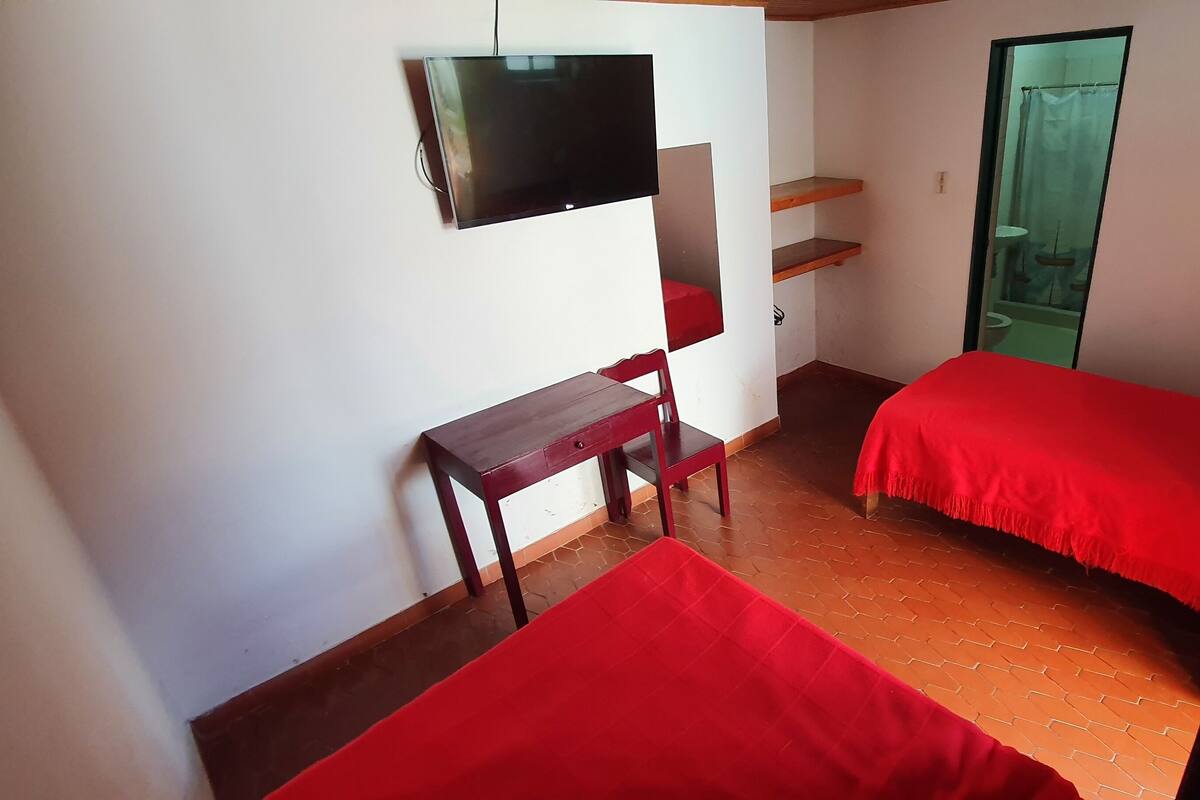 Una habitación pequeña con una cama, un escritorio, una silla y un televisor montado en la pared.