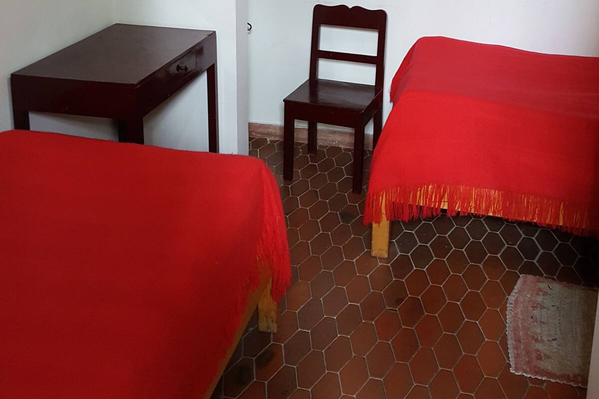 Una habitación con dos camas, un escritorio, una silla y un televisor fijado a la pared.