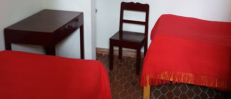Una habitación con dos camas, un escritorio, una silla y un televisor fijado a la pared.