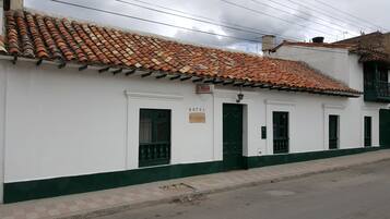 Un edificio blanco con techo de tejas y puertas verdes, con la señalización