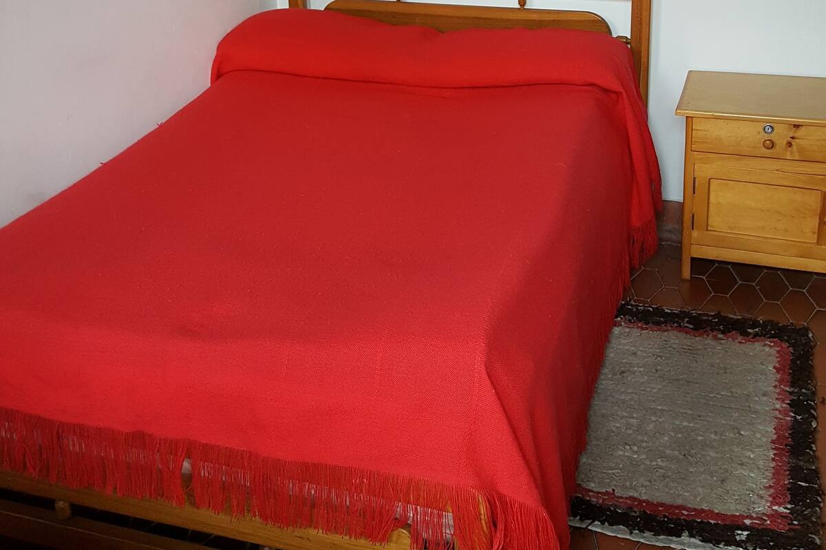 Una habitación con una cama de madera, una mesita de noche de madera y piso de baldosas.