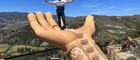 A person standing on a large hand sculpture with a mountainous landscape in the background.