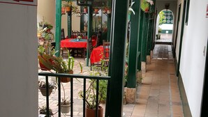 A corridor with a red table and chairs, potted plants, and a sign reading "SALIDA". - Hotel La Posada (Paipa)