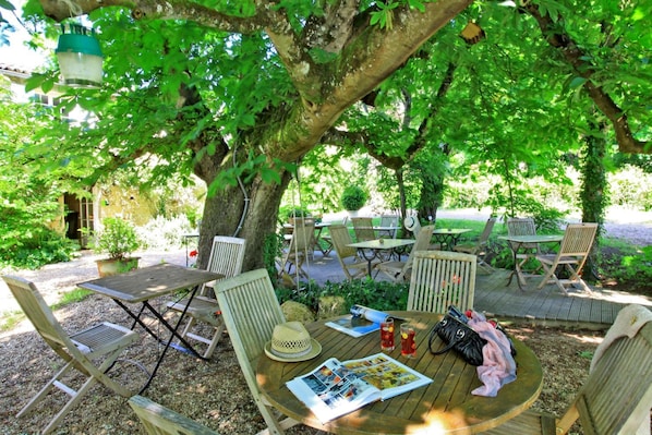 An outdoor seating area with wooden tables and chairs, surrounded by trees. - Hotel Maison des Peyrat (Sarlat-la-Canéda)