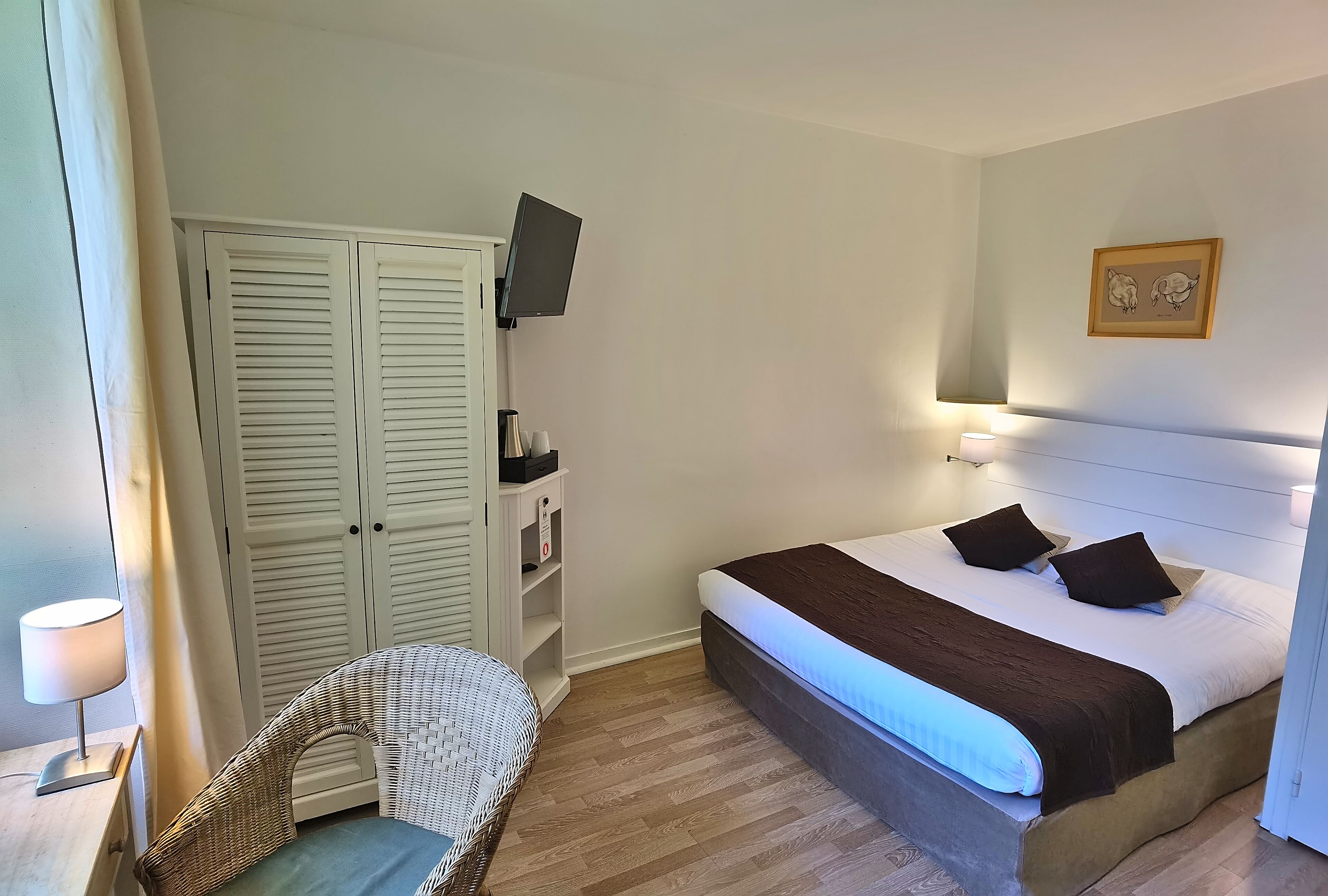 A bedroom with a bed, a chair, a wardrobe, a TV, and a wall-mounted picture.