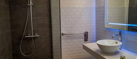 A modern bathroom with a glass-enclosed shower, a white sink, and a mirror with LED lighting.