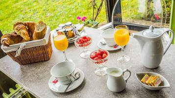 Desayuno con cruasanes, fruta, jugo de naranja y café sobre una mesa con vista a follaje.