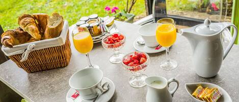 Desayuno con cruasanes, fruta, jugo de naranja y café sobre una mesa con vista a follaje.