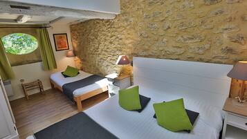 A bedroom with a stone wall, two beds, green pillows, and a window with a view.