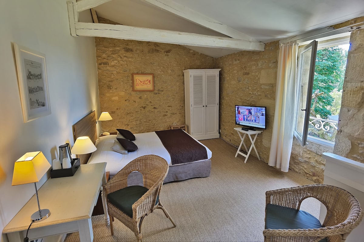 Una habitación con cama, dos sillas, escritorio, televisión y ventana con cortinas.