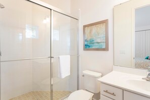 Un baño moderno con cabina de ducha de vidrio, inodoro blanco y lavamanos con espejo.