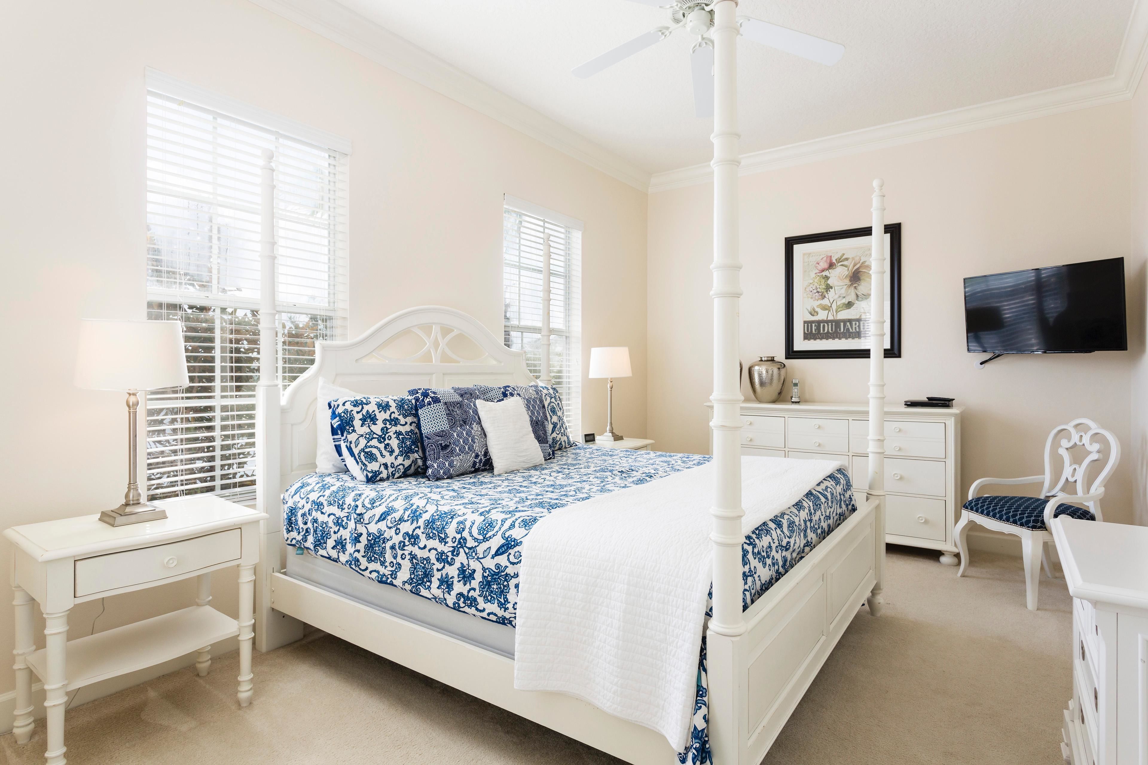 A bedroom with a four-poster bed, a nightstand, a chair, a dresser, a television, and a window with blinds.