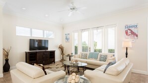 A spacious living room with a flat-screen TV, a glass coffee table, and a beige sofa. - Villa The Nantucket at Patriots Landing 3 Bedroom Reunion (Kissimmee)
