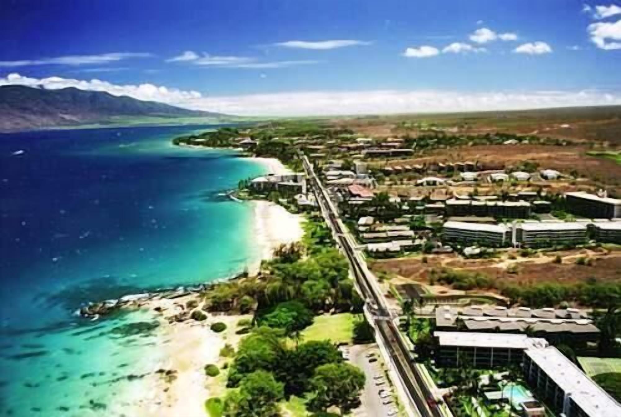 An aerial view of a coastal area with a beach, buildings, and a road.