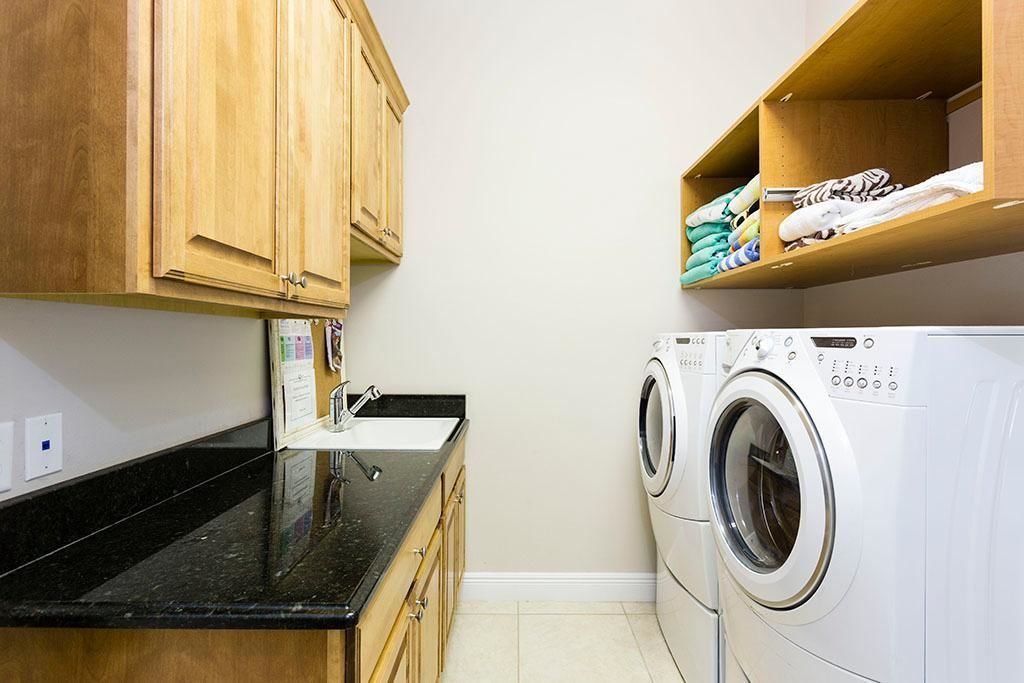 A laundry area with a washing machine and a sink, wooden cabinets, and a shelf with folded clothes.