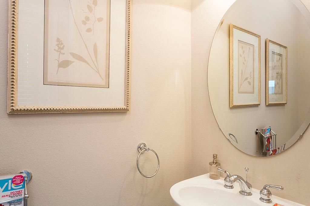 A bathroom with a round mirror, framed artwork, a sink with two faucets, and a hand towel ring.