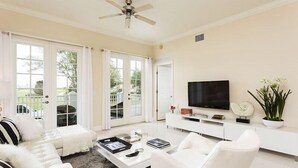 Un salon moderne avec un canapé blanc, une table basse, un téléviseur et une plante en pot.