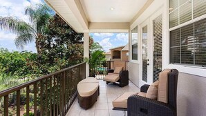 A balcony with wicker furniture, a view of a pool, and lush greenery.