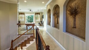 A spacious hallway with a wooden staircase, a decorative wall, and a view of the living area.