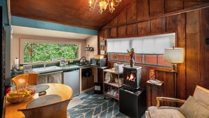 A cozy cabin interior with a wooden interior, a kitchen area, a dining table, and a fireplace. - Volcano Artist Cottage (Volcano)