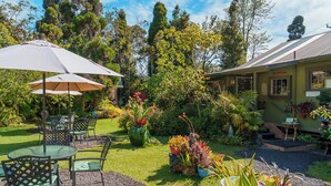 A garden area with outdoor seating, a building with an entrance sign, and various plants. - Volcano Artist Cottage (Volcano)