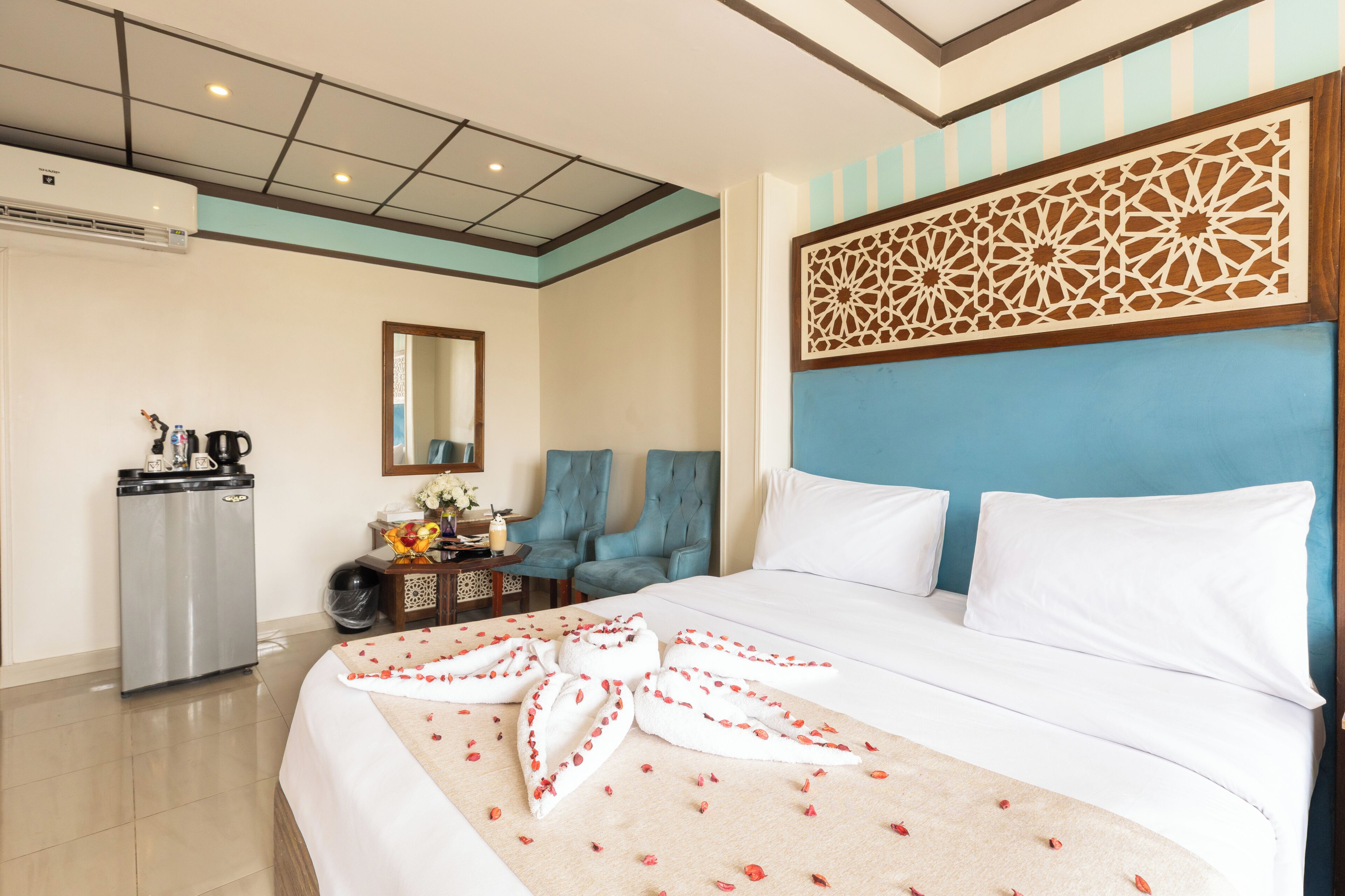 A hotel room with a large bed, a desk with a coffee maker, two armchairs, and a decorative headboard.