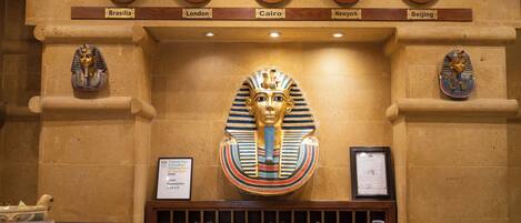 A reception desk with clocks displaying times in various cities, a large Egyptian sarcophagus, and framed certificates.