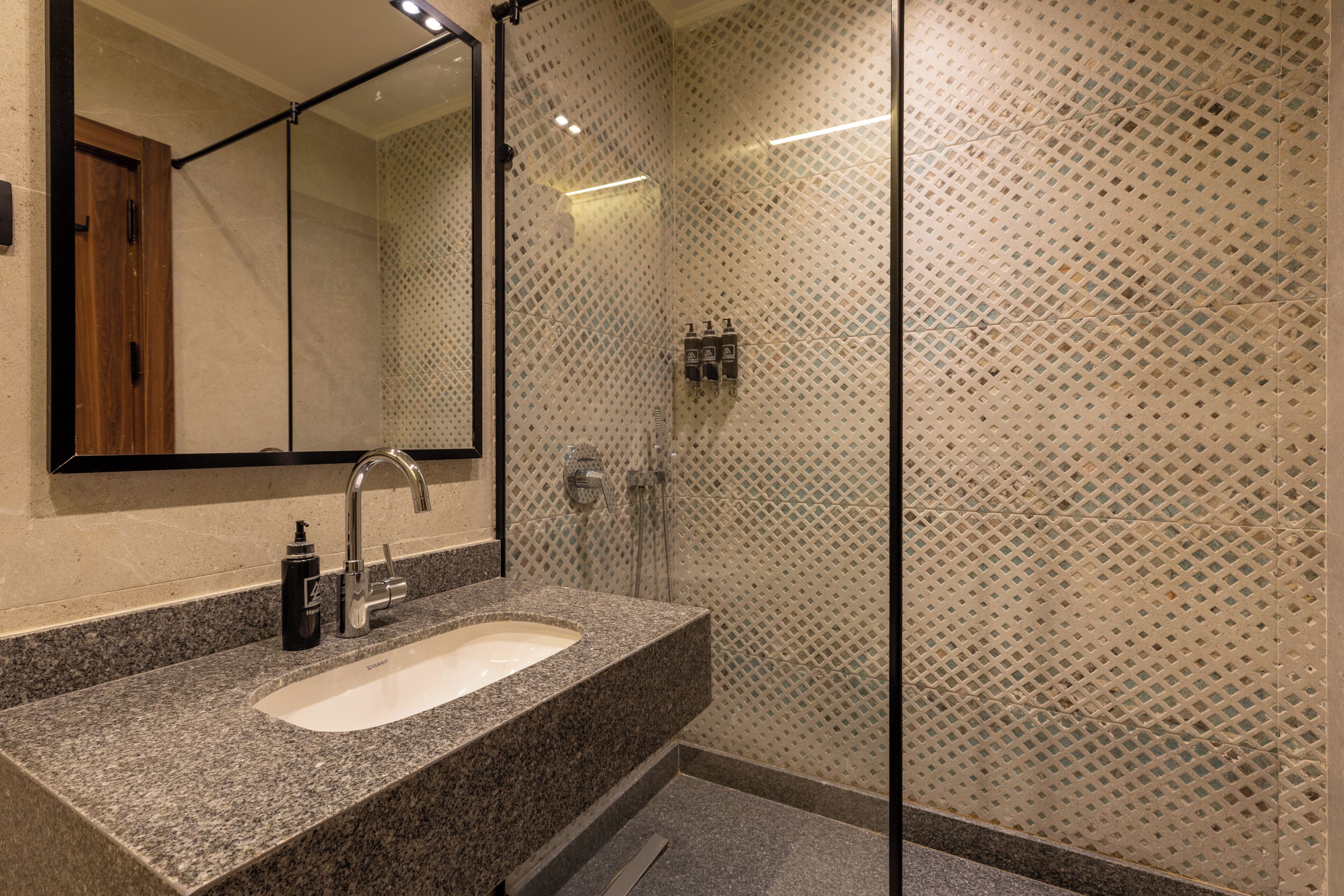 Ein Badezimmer mit einer Granitplatte, einem Waschbecken, einem Spiegel und einer Dusche mit einer Wandverkleidung.
