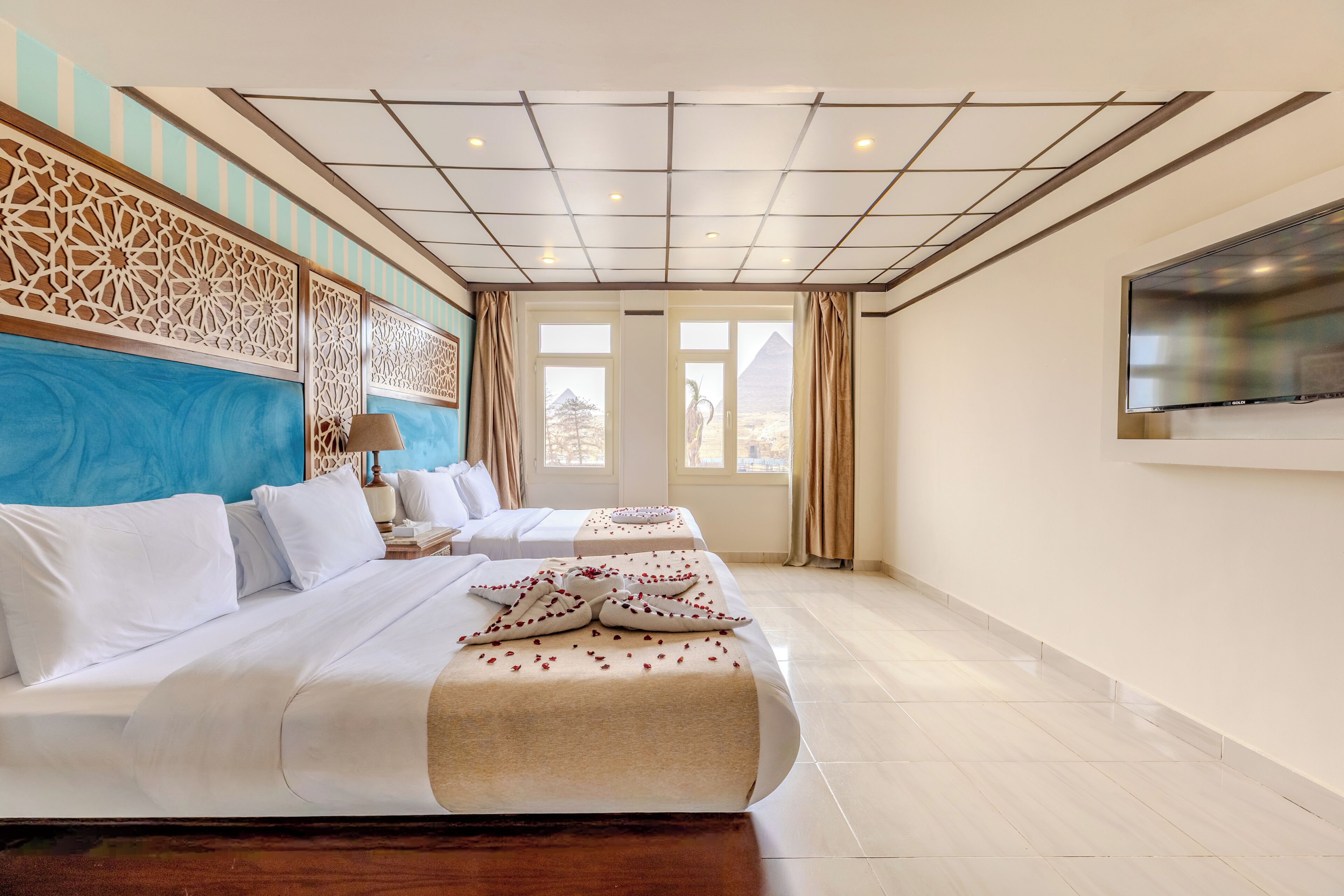 A hotel room with two beds, a large TV, and a view of the pyramids.