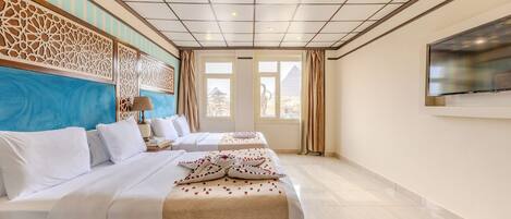 A hotel room with two beds, a large TV, and a view of the pyramids.