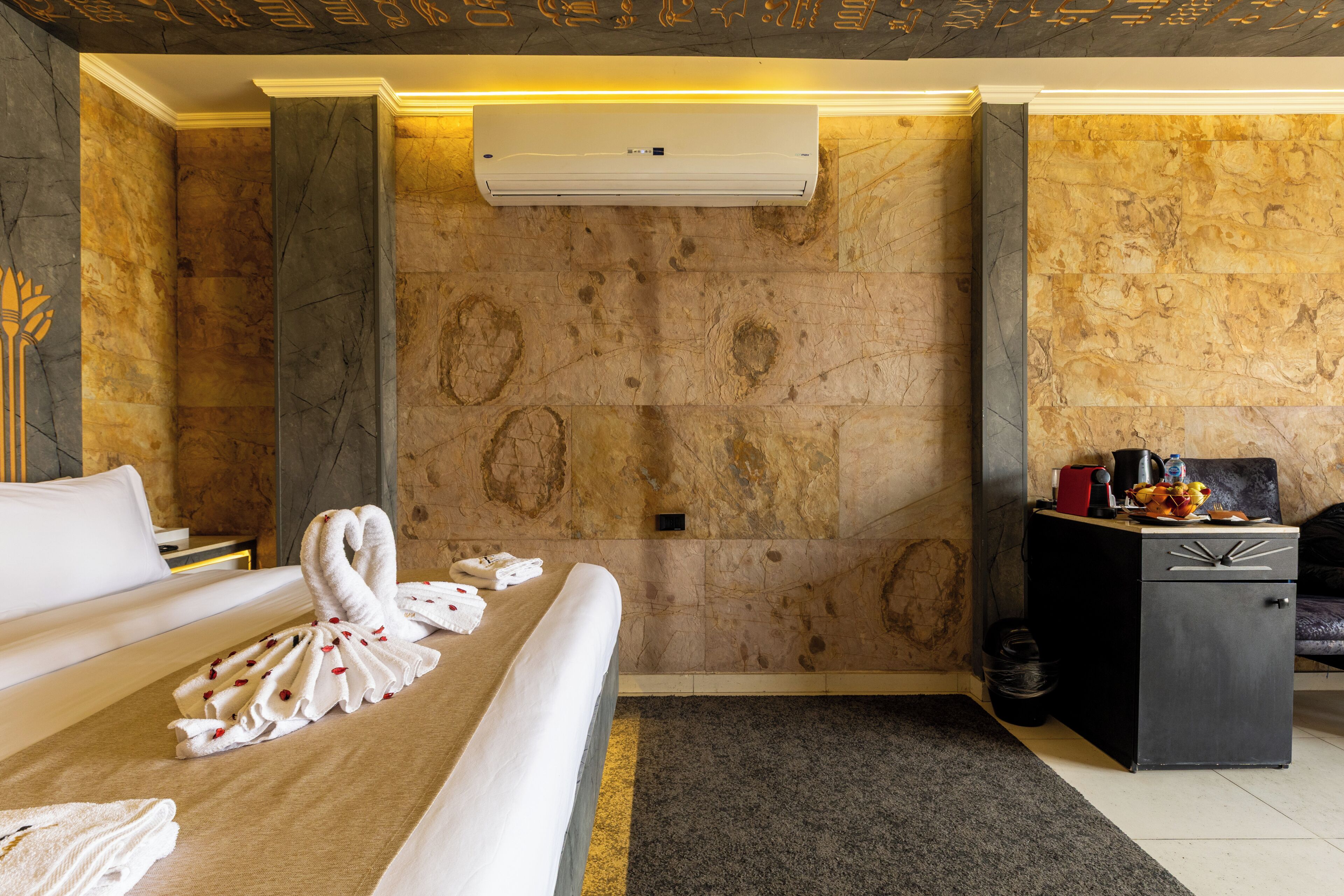 A hotel room with a bed, a desk, a chair, an air conditioning unit, and a wall with a marble-like texture.