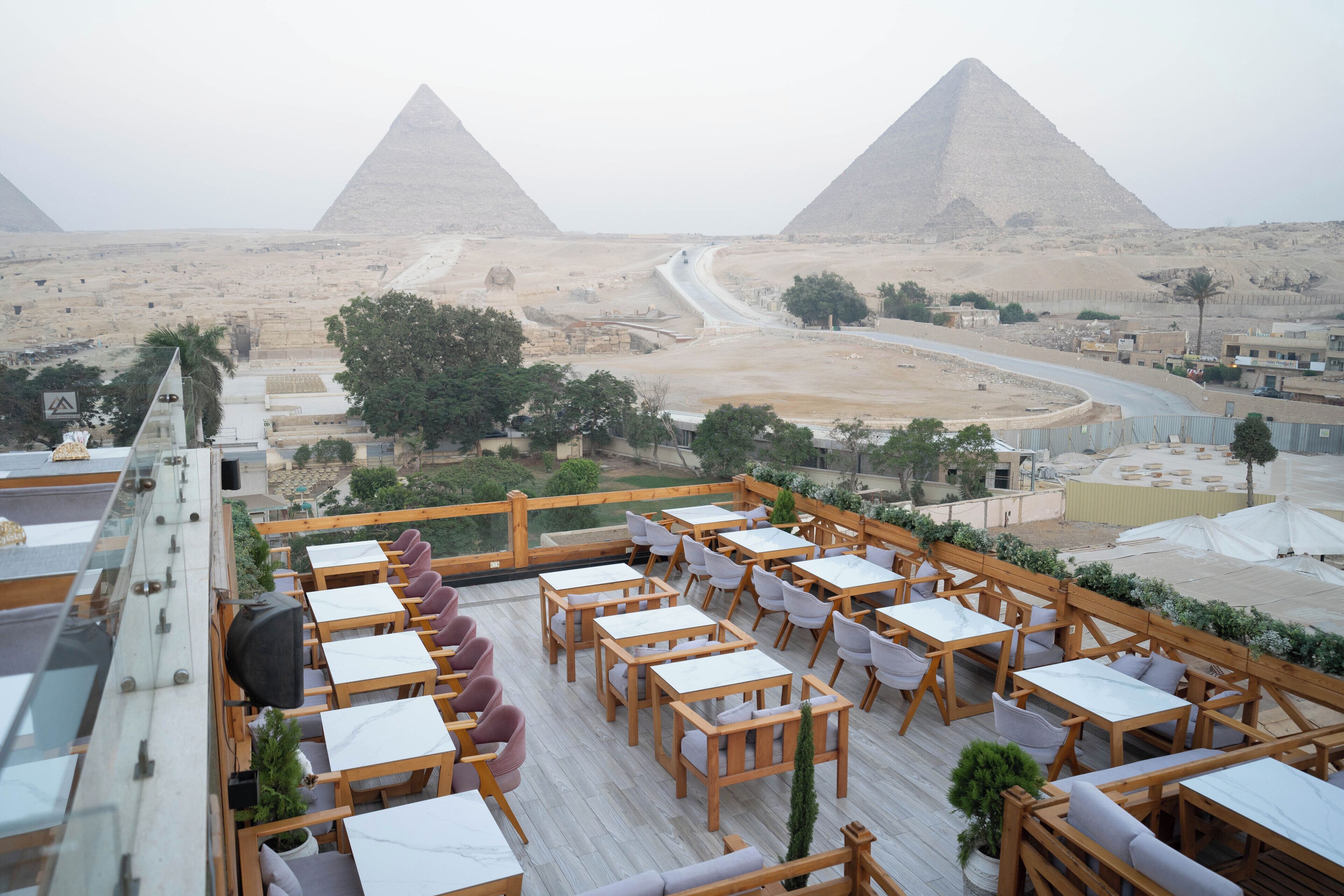 A rooftop terrace with wooden tables and chairs, offering a view of the pyramids.