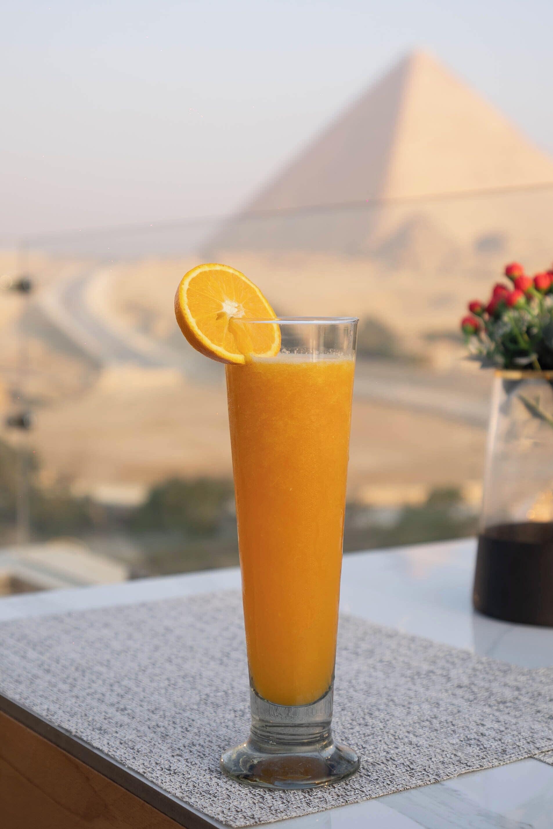 Een hoog glas sinaasappelsap met een schijfje sinaasappel op de rand, geplaatst op een geribbelde mat.