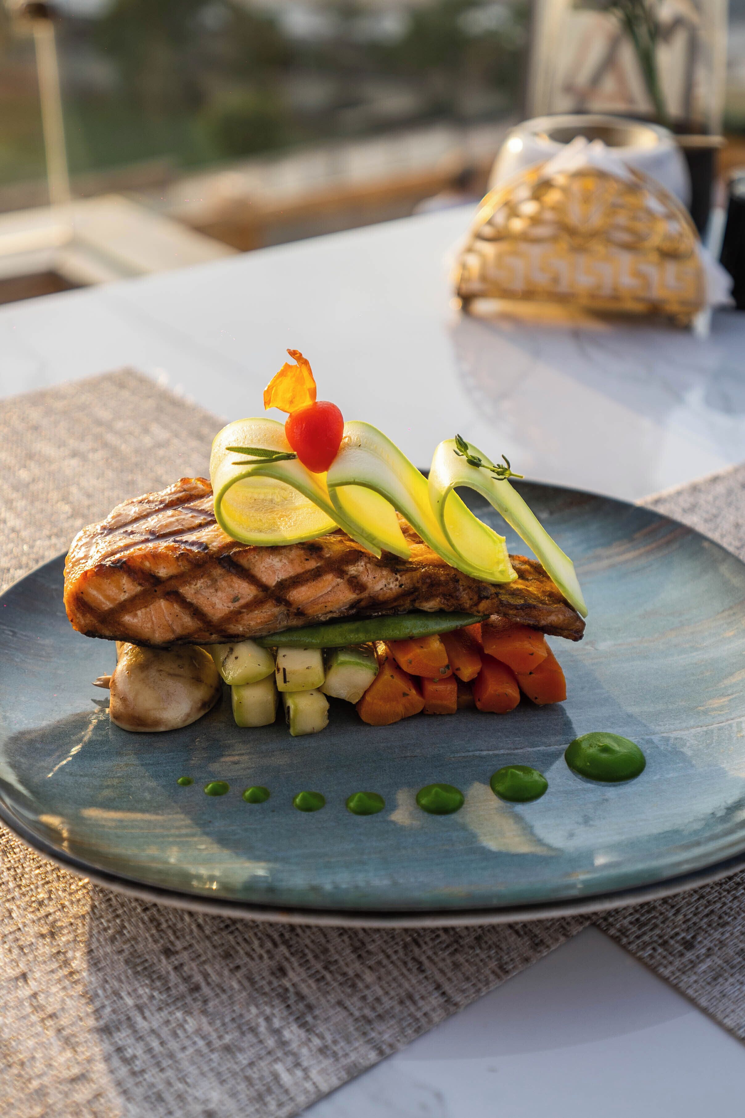 A plate with grilled salmon, vegetables, and a garnish on a table.