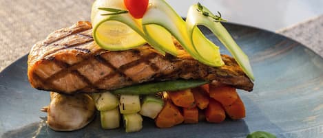 A plate with grilled salmon, vegetables, and a garnish on a table.