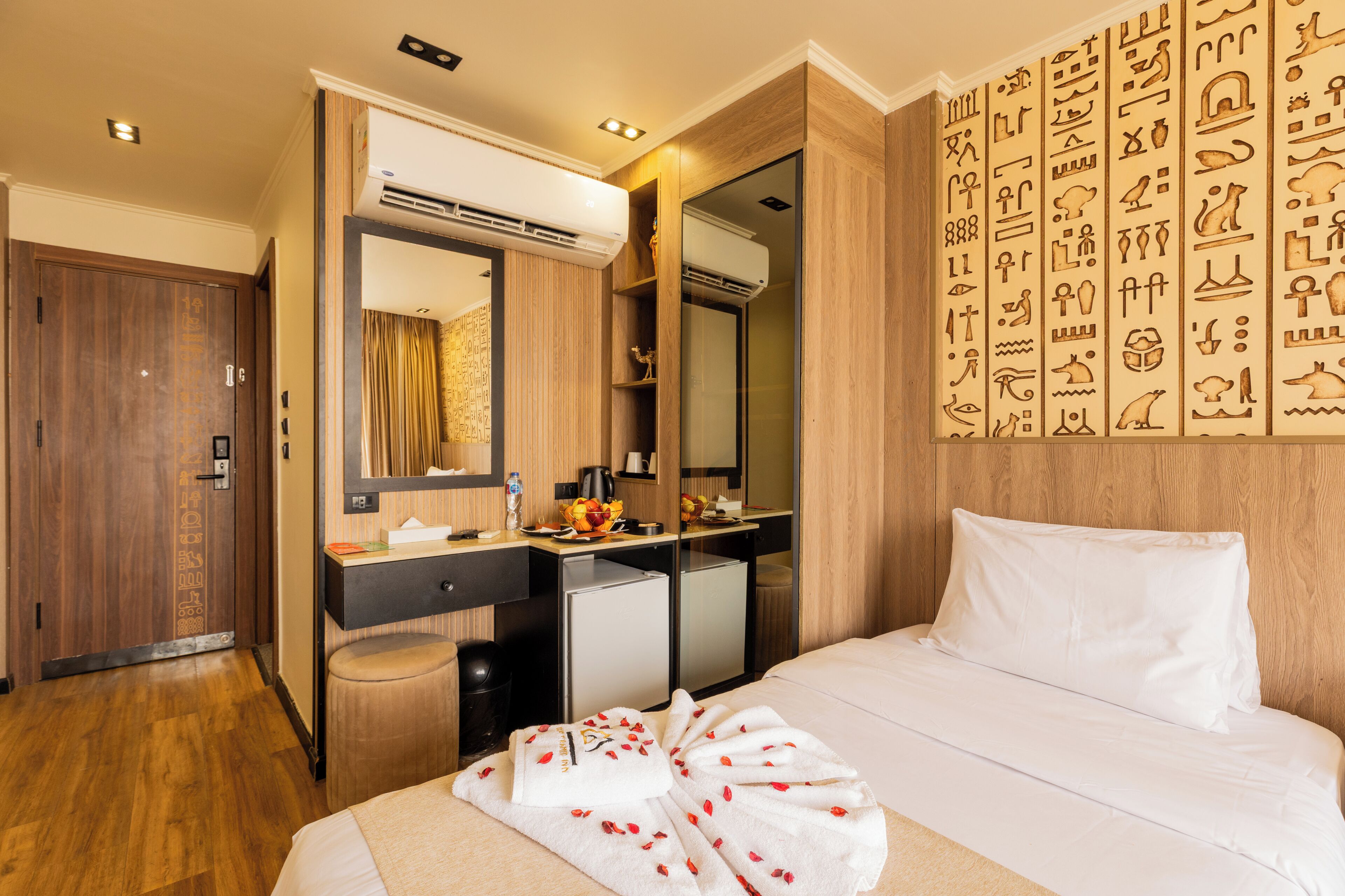 A hotel room with a bed, a desk with a computer, a minibar, and a large mirror.