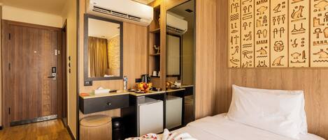 A hotel room with a bed, a desk with a computer, a minibar, and a large mirror.
