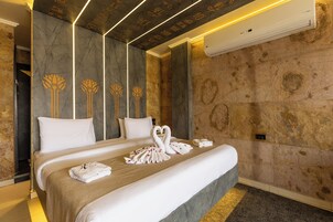 Habitación de hotel con una cama grande, dos almohadas, aire acondicionado de pared y una presentación de toallas sobre la cama.