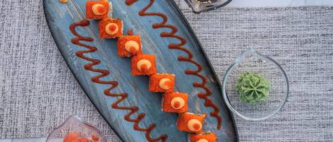 A blue plate with sushi pieces arranged in a line, accompanied by small bowls of sauce and pickled vegetables.