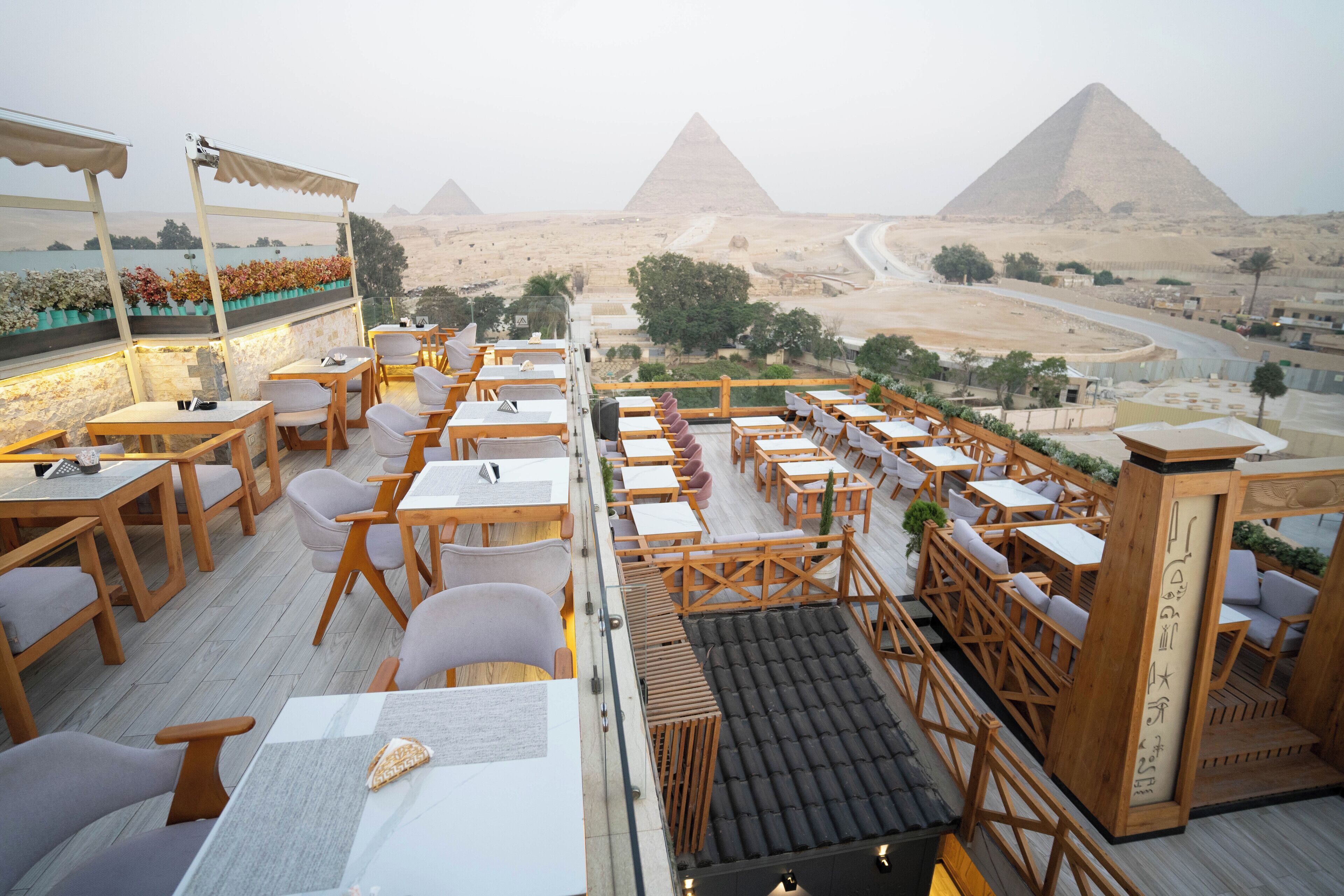 A rooftop restaurant with tables and chairs, offering a view of the pyramids.
