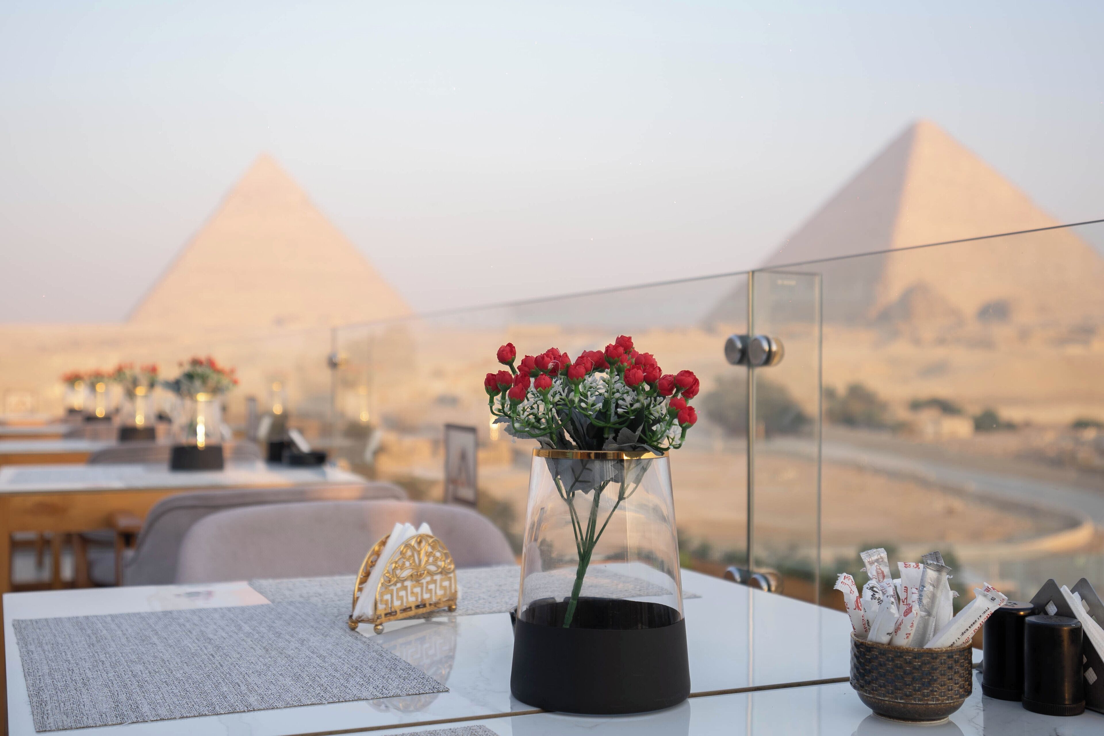 A table with a vase of red flowers, a small basket of items, and a view of the pyramids in the background.